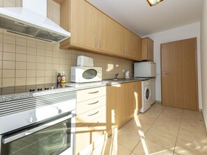 A kitchen with wooden cabinets, a microwave, a washing machine, and a countertop with a sink. - Beachside Bliss 5 mins Beach & Waterfront - Pool - Wi-Fi (Cabanas de Tavira)