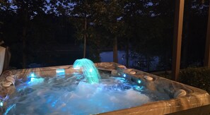 Een bubbelbad met een waterval, omringd door bomen en een overdekt terras.
