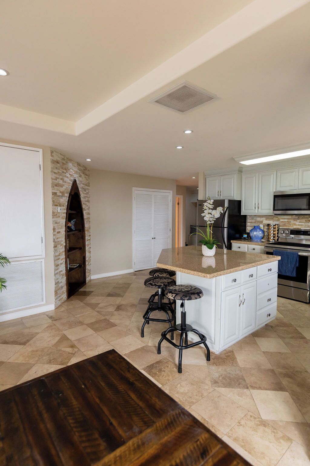 A spacious kitchen with a central island, white cabinetry, and a stone accent wall.