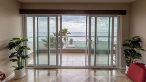A spacious room with a large sliding glass door leading to a balcony with a view of the ocean.