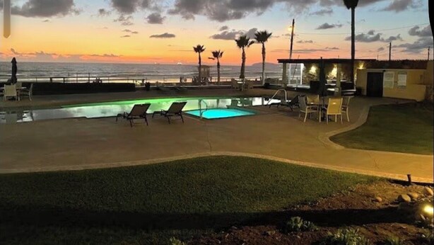 A pool area with lounge chairs, a small building, and palm trees.
