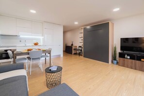 A modern living space with a kitchen, dining area, and a seating area with a TV and entertainment unit. - Modern Open-Plan Studio with Garage by HostWise (Porto)