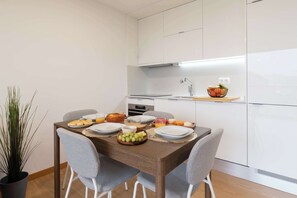 A modern kitchen with white cabinets, a wooden dining table set with plates, bowls, and a fruit bowl. - Modern Open-Plan Studio with Garage by HostWise (Porto)