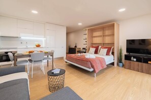 A modern, well-lit room with a bed, a TV, a dining area, and a kitchen. - Modern Open-Plan Studio with Garage by HostWise (Porto)