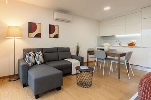 A modern living room with a grey sofa, a round coffee table, and a dining area with a wooden table and chairs. - Modern Open-Plan Studio with Garage by HostWise (Porto)