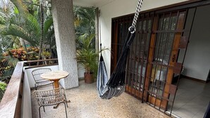 Een balkon met een hangmat, een tafel met stoelen en planten in potten.