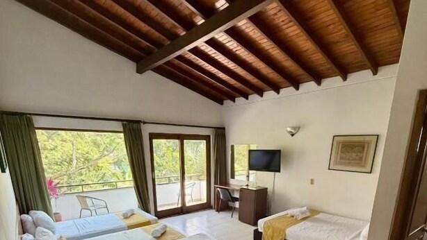 Een hotelkamer met twee bedden, een bureau, een televisie en een balkon met uitzicht op groen.