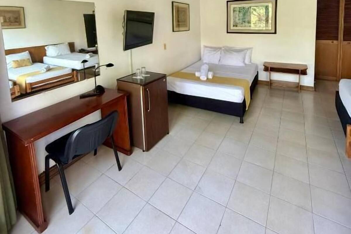 Une chambre d’hôtel avec un plafond en bois, un lit, un bureau avec une chaise, une télévision et une petite table.