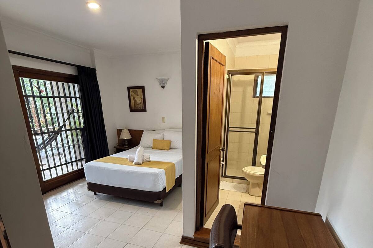 Une chambre d’hôtel avec un lit, un bureau et une salle de bain, visibles à travers une porte ouverte.