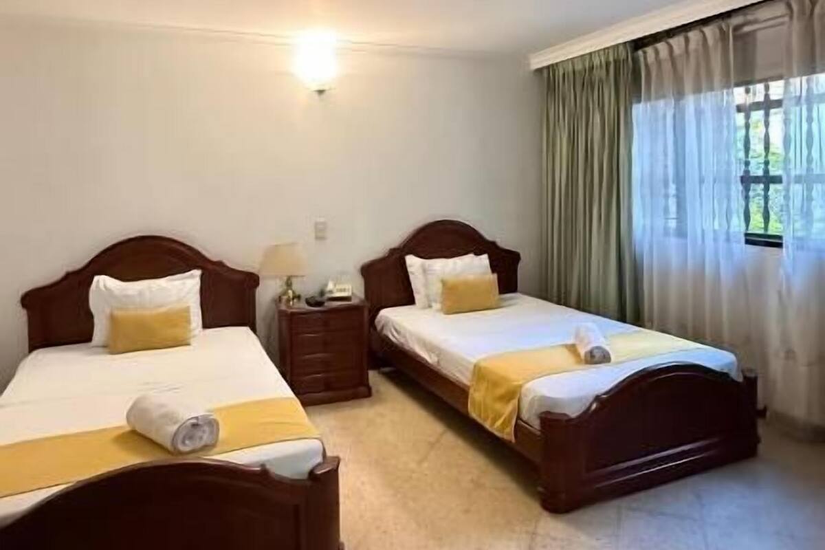 Une chambre d’hôtel avec deux lits en bois, une table de chevet avec une lampe et une fenêtre avec des rideaux.