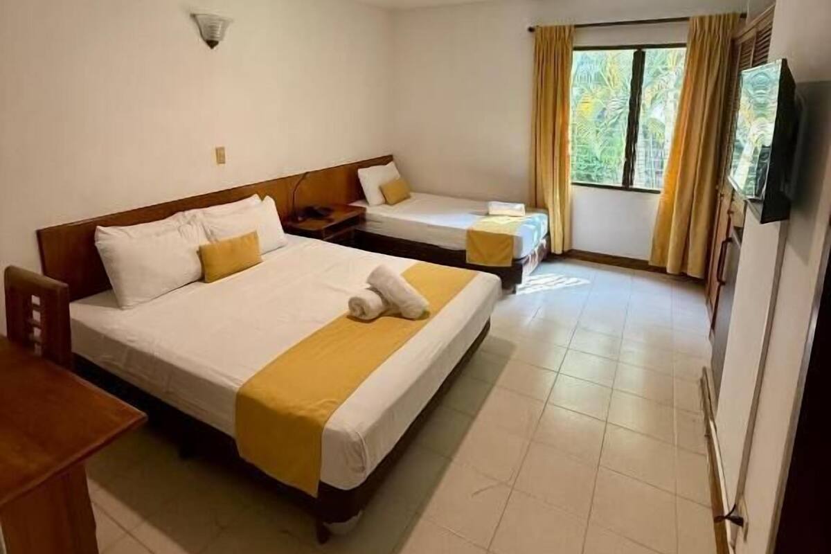 Une chambre d’hôtel avec deux lits, une petite table, un téléviseur et une fenêtre avec des rideaux.