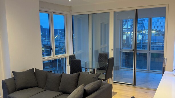 Una sala de estar moderna con un sofá seccional, una mesa de comedor y sillas. Se ve un ventanal con vistas a la ciudad.