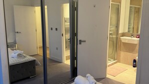 Habitación de hotel con un gran ventanal corredero que da a un área de ducha, una cama con una toalla enrollada y una mesita de noche.
