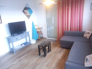Ein Wohnzimmer mit einer Couch, einem Fernseher auf einem Schrank, einem kleinen Tisch und einem Sessel.