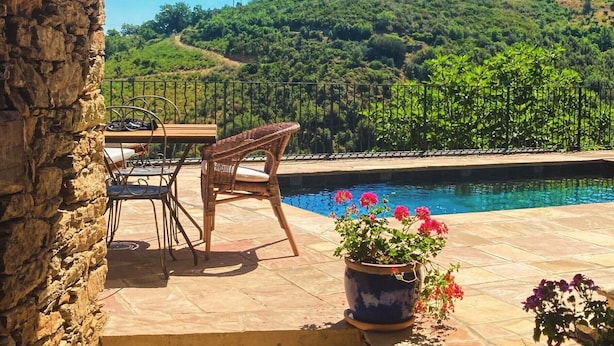 Un muro de piedra, una piscina, sillas y vistas a una ladera verde.