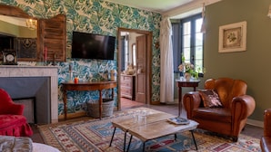Una habitación con chimenea, televisor, un sillón rojo, un tapete estampado y una puerta que da a otra estancia.