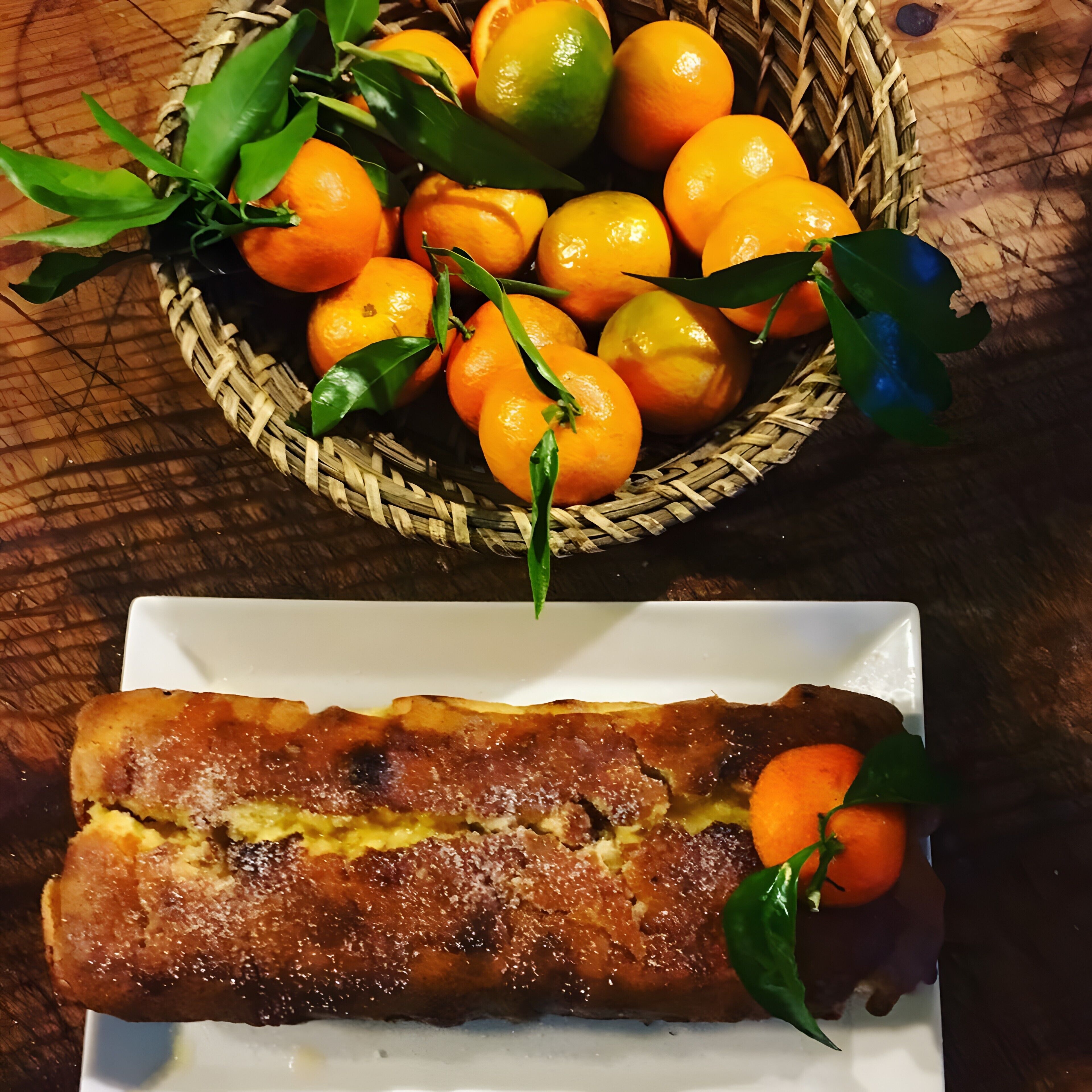 Una cesta tejida llena de naranjas y un plato con un pastel horneado.