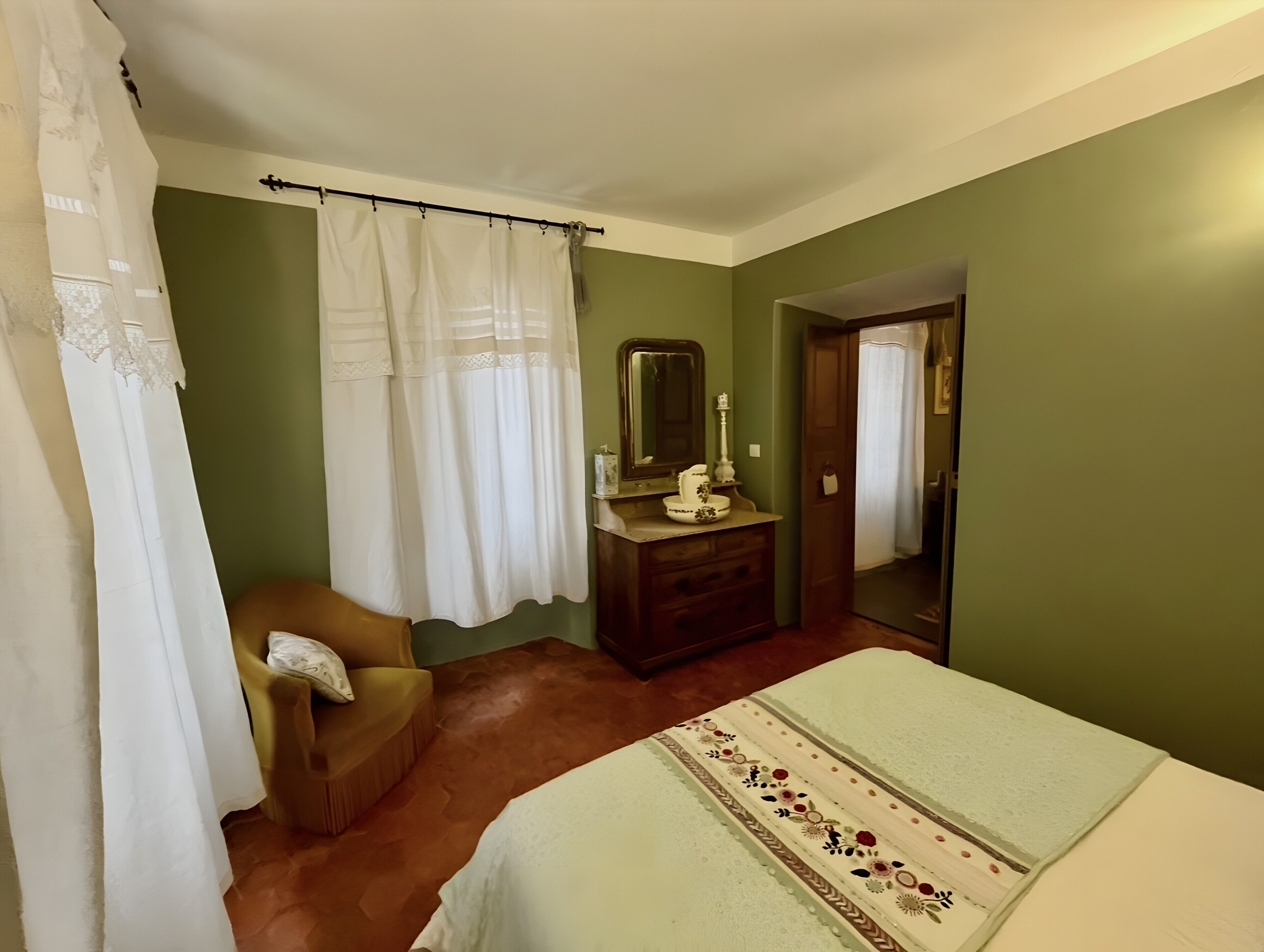 A bedroom with a bed, a chair, a dresser, a mirror, and a door.