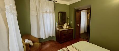 A bedroom with a bed, a chair, a dresser, a mirror, and a door.