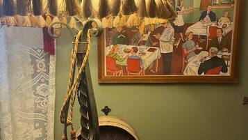 Une pièce comprenant une table à manger, un radiateur fixé au mur et un tableau représentant une scène de repas.