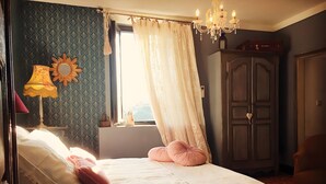 A bedroom with a bed, a nightstand, a lamp, a window with curtains, a chandelier, and a wardrobe. - Signoretta-Casa ghjunca Guest Room (Rapale)