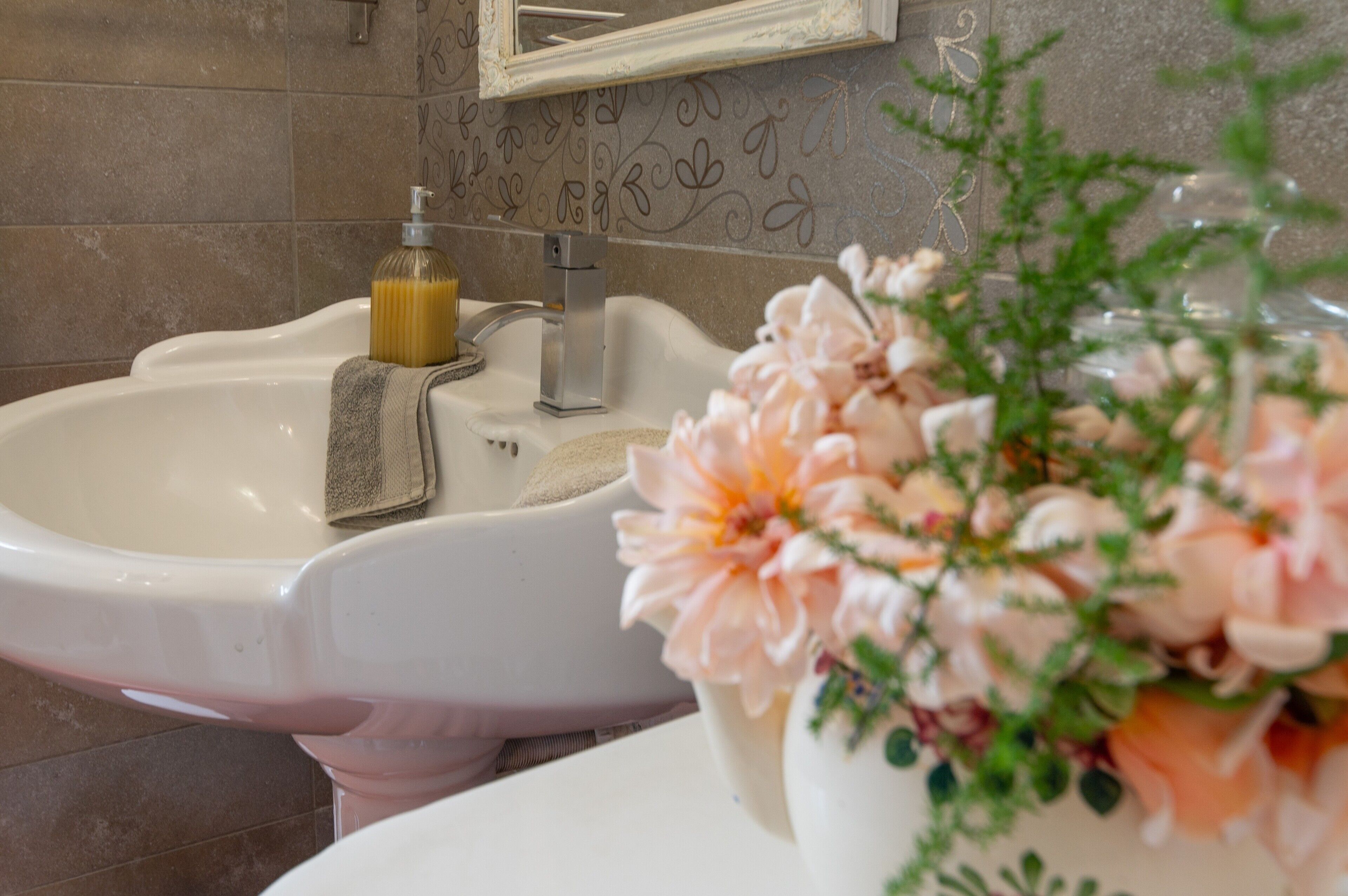 Une salle de bain équipée d’un lavabo, d’un miroir et d’un arrangement floral décoratif.