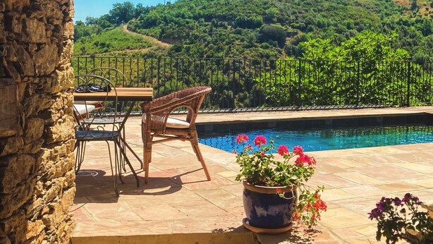 Un mur de pierre, une piscine, des chaises et une vue sur une colline verdoyante.