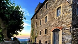 Un bâtiment en pierre doté de nombreuses fenêtres, d’une porte et d’un espace extérieur aménagé pour s’asseoir.