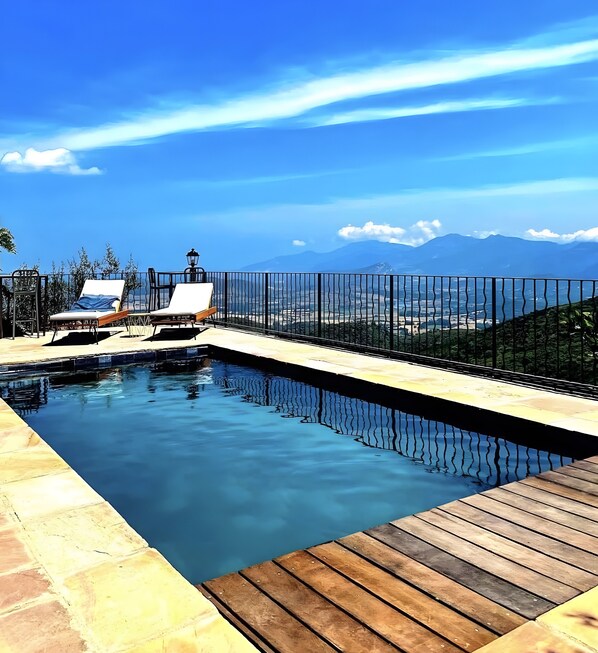 A swimming pool with a wooden deck, lounge chairs, and a view of mountains.