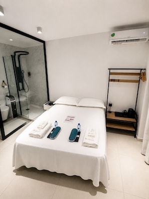 A hotel room with a bed, a bedside table, a mirror, a shower, and a wardrobe.