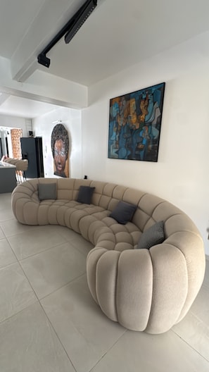 A modern living room with a curved sectional sofa, a large abstract painting, and a tiled floor.