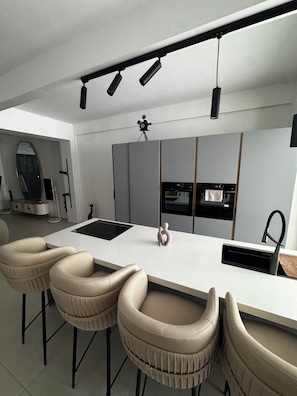 A modern kitchen with a central island, bar stools, a tripod-mounted camera, and a built-in oven.