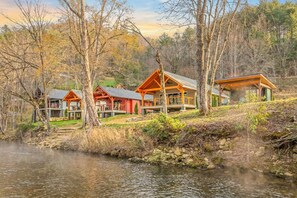 A lakeside cabin with a deck, a covered porch, and a separate building with a large window. - Rose Cabin at Highland Peaks Retreat (Highlands)