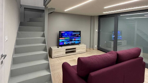 A modern living room with a staircase, a flat-screen TV, and a red sofa. - Dante Urbano Loft (Torino)