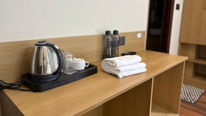 A hotel room with a wooden desk, a kettle, a tray with glasses and a mug, and a stack of towels. - Hotel Abline The Oaks (Rishikesh)