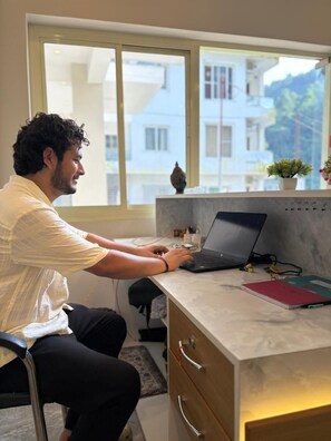 A person working at a desk with a laptop, a notebook, and a potted plant. - Hotel Abline The Oaks (Rishikesh)
