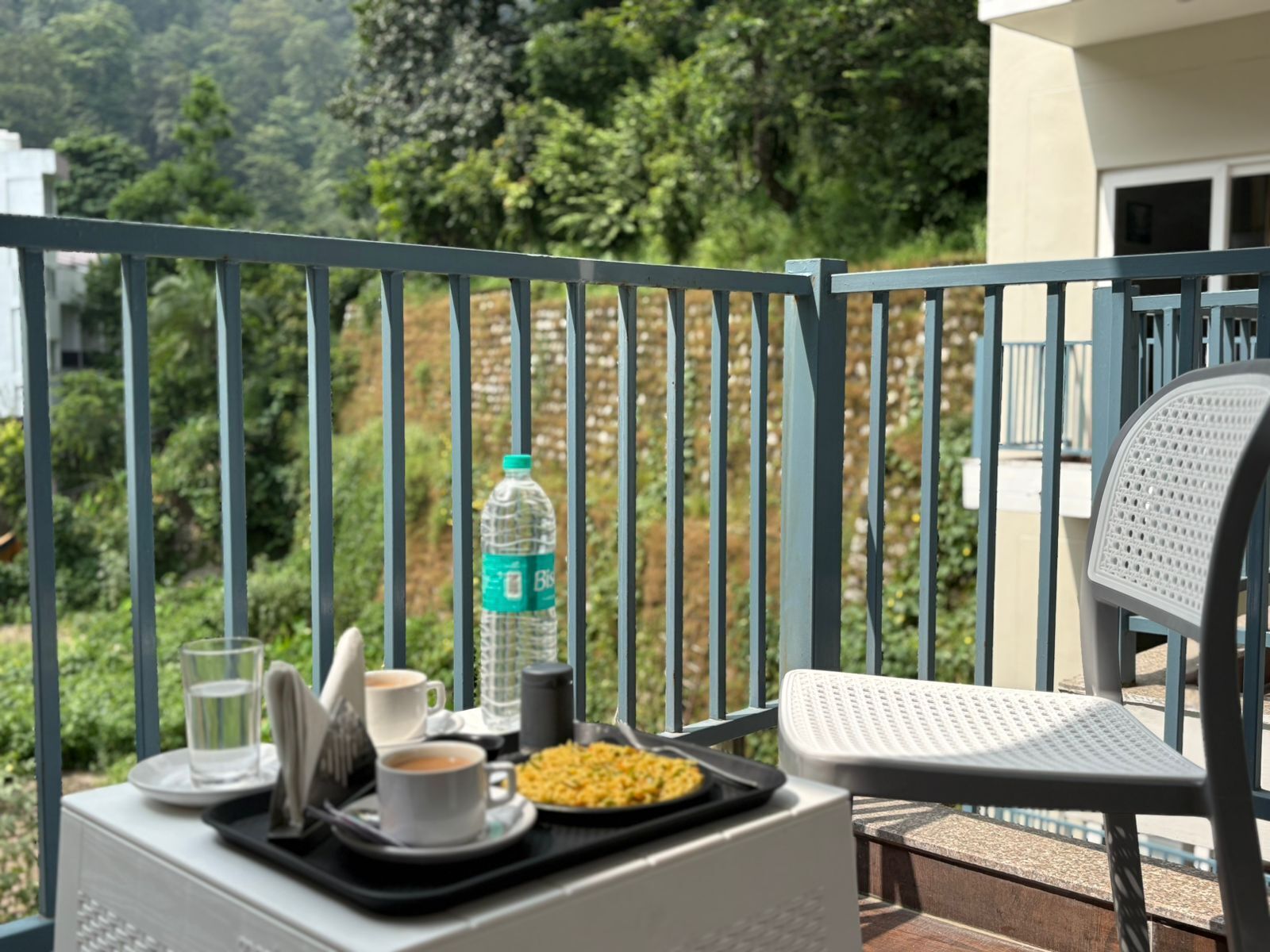 En balkon med et bord dækket til et måltid, inklusive en vandflaske, en kop kaffe og en tallerken med mad.