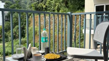 En balkon med et bord dækket til et måltid, inklusive en vandflaske, en kop kaffe og en tallerken med mad.