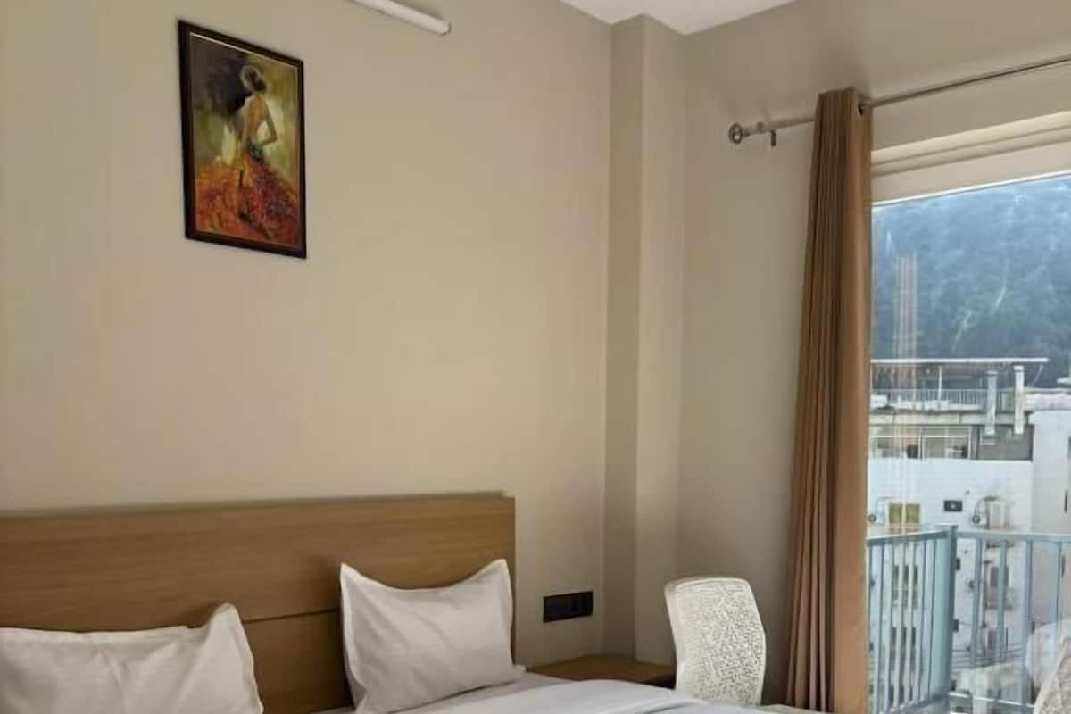 Una habitación de hotel con una cama grande, un cuadro en la pared, una ventana con cortinas y vistas a edificios.