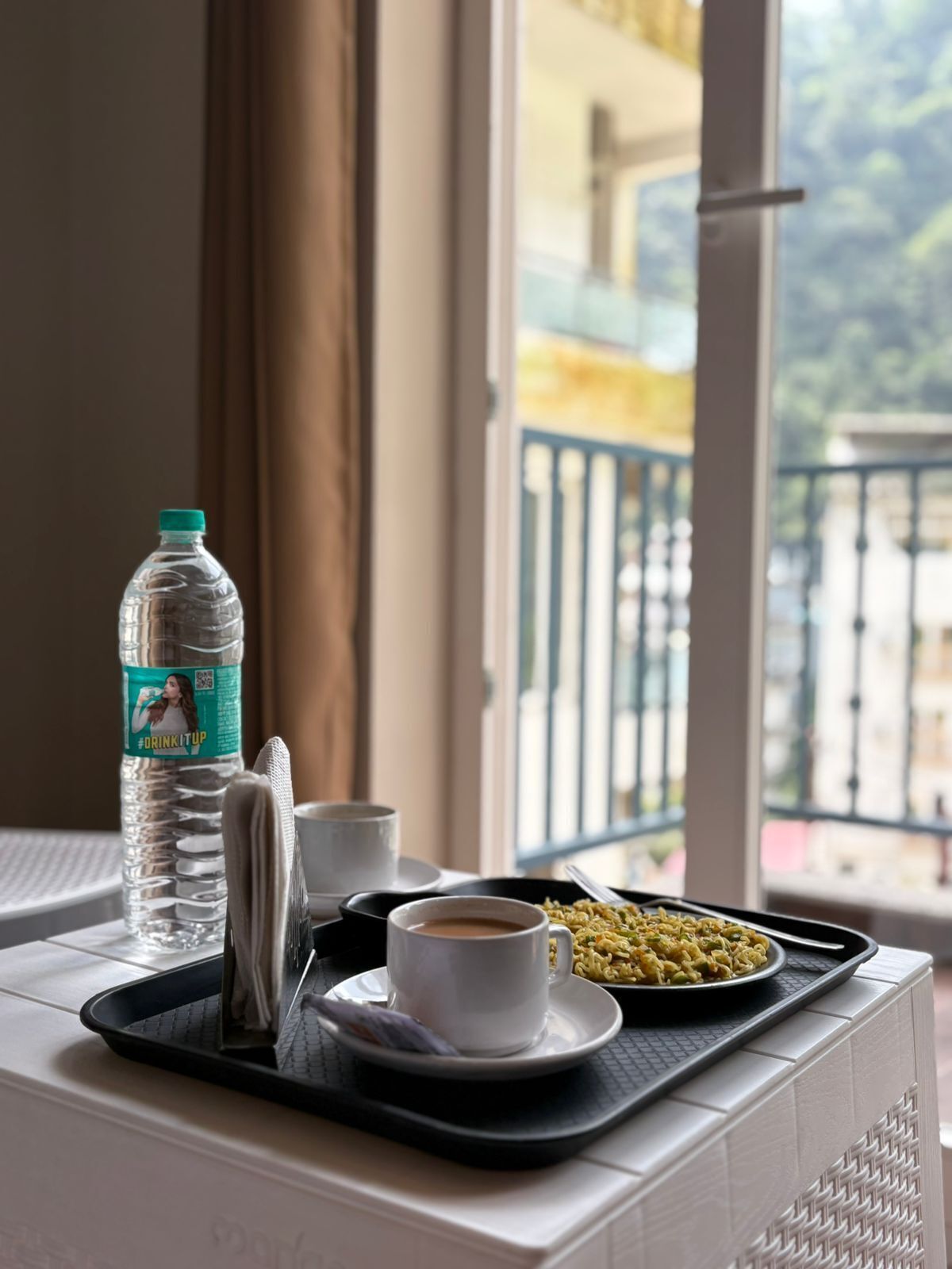 Una bandeja con una botella de agua, una taza de café y un plato de comida sobre un alféizar.
