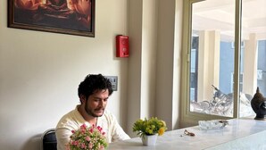 A person seated at a marble reception desk with a Buddha painting above, a small Buddha statue, and a window with a view. - Hotel Abline The Oaks (Rishikesh)