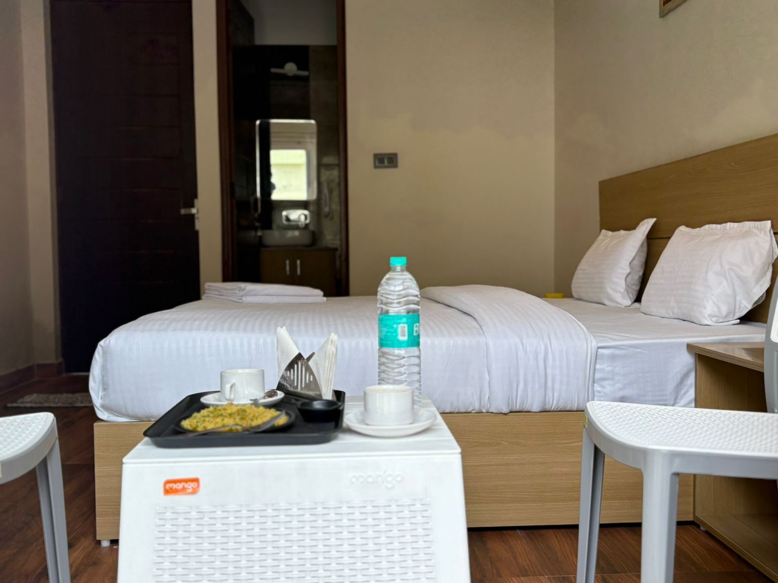 Habitación de hotel con una cama, una mesita con una botella de agua, una taza y una bandeja con comida.