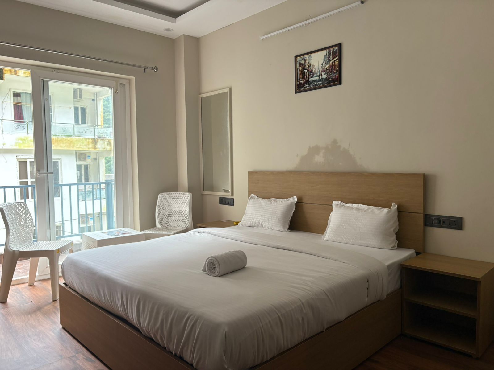 Quarto de hotel com uma cama grande, uma cadeira, uma escrivaninha e uma varanda com vista para edifícios.