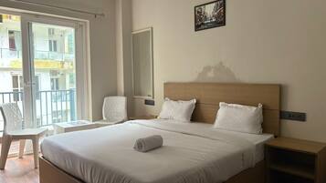 Quarto de hotel com uma cama grande, uma cadeira, uma escrivaninha e uma varanda com vista para edifícios.