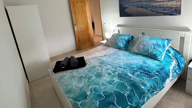 A bedroom with a bed, a painting of birds flying over water, a ceiling fan, and a wooden door. - Renovated apartment with pool and 2 minutes from the beach. Quiet location (Els Muntells)