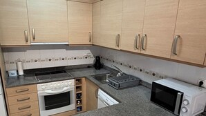 A kitchen with wooden cabinets, a built-in oven, a microwave, and a sink. - Renovated apartment with pool and 2 minutes from the beach. Quiet location (Els Muntells)