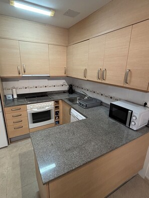 A kitchen with wooden cabinets, a built-in oven, a microwave, and a sink. - Renovated apartment with pool and 2 minutes from the beach. Quiet location (Els Muntells)