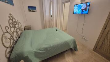 Una camera da letto con un letto, una televisione a muro e una finestra con tende.