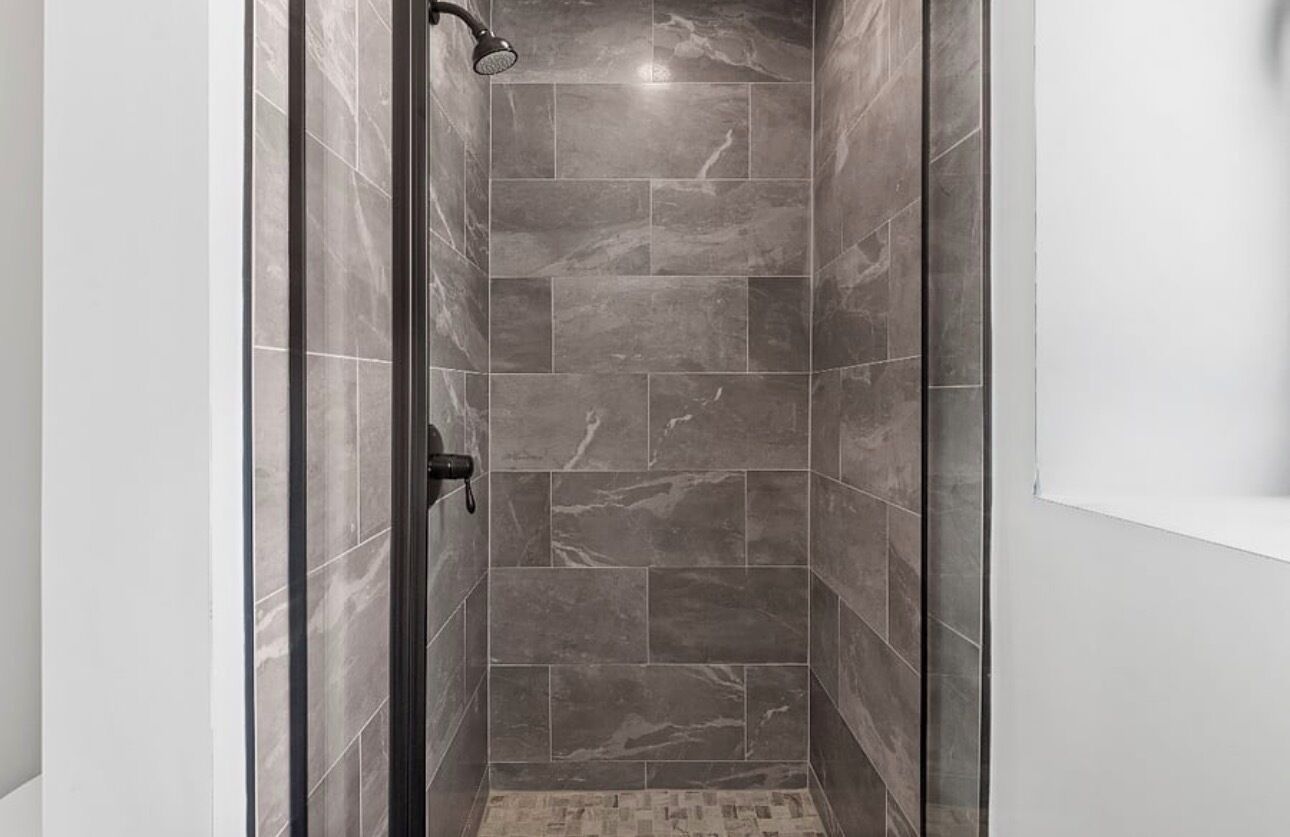 A narrow shower stall with dark tiles and a handheld showerhead.