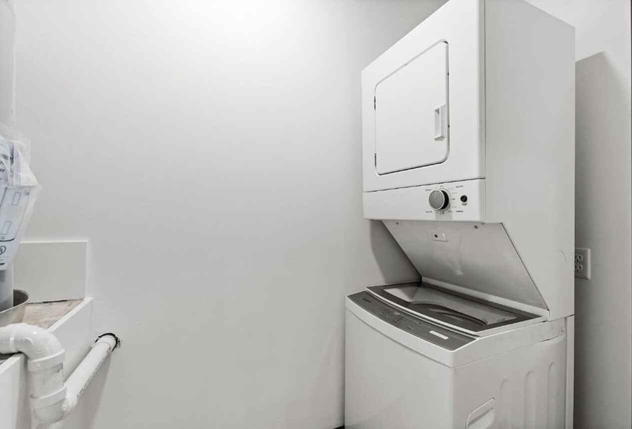 Een kleine, moderne wasruimte met een ingebouwde wasmachine en droger, een klein prullenbakje en een handdoekhouder.